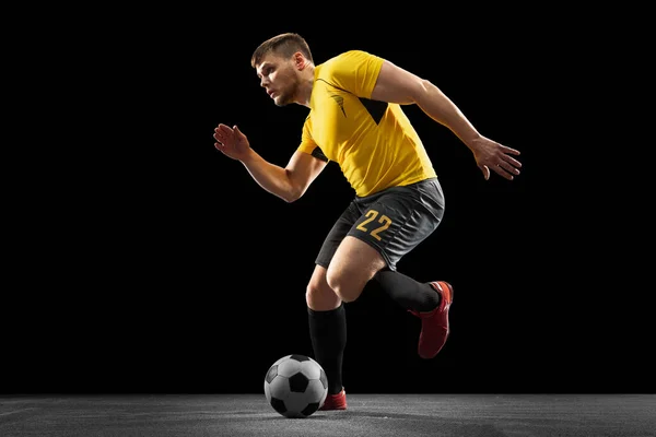 Poderoso, volando sobre el campo. Fútbol joven, jugador de fútbol en acción, movimiento aislado en el fondo negro del estudio . — Foto de Stock
