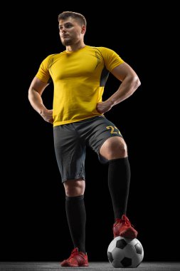 Siyahi stüdyo arka planında tek başına duran profesyonel beyaz futbolcu..