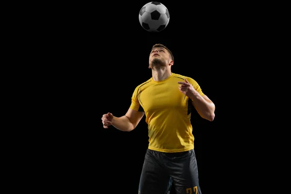 Poderoso, voando acima do campo. Jovem futebol, jogador de futebol em ação, movimento isolado no fundo do estúdio preto . — Fotografia de Stock