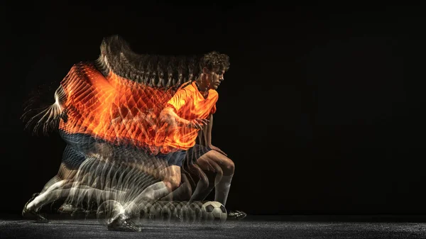 Ein kaukasischer Fußballspieler in Bewegung und Aktion in gemischtem Licht auf dunklem Hintergrund. — Stockfoto