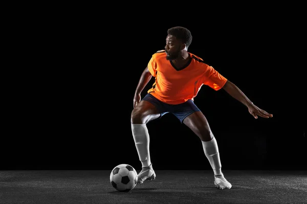 Genç Afrikalı futbolcu siyah arka planda tek başına oynuyor. Spor, hareket, enerji ve dinamik kavramı. — Stok fotoğraf
