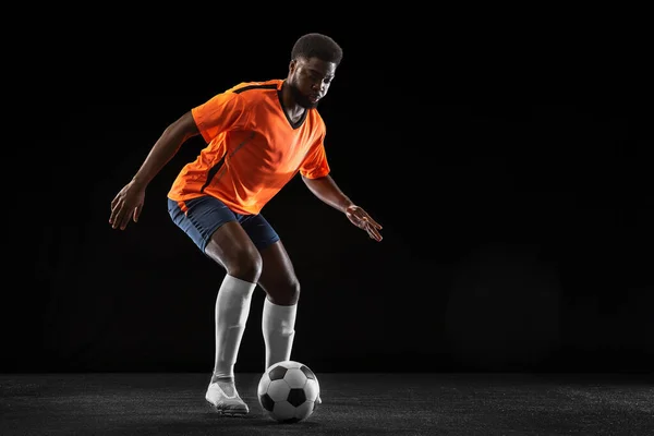 Jovem jogador de futebol africano jogando isolado em fundo preto. Conceito de esporte, movimento, energia e dinâmica. — Fotografia de Stock