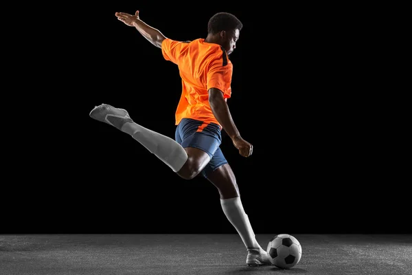 Jovem jogador de futebol africano jogando isolado em fundo preto. Conceito de desporto. — Fotografia de Stock