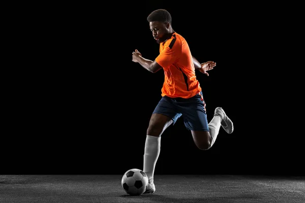 Młody afrykański piłkarz grający na czarnym tle. Pojęcie sportu, ruchu, energii i dynamiki. — Zdjęcie stockowe