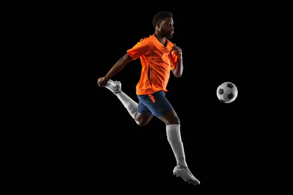 Jovem jogador de futebol africano jogando isolado em fundo preto. Conceito de esporte, movimento, energia e dinâmica. — Fotografia de Stock