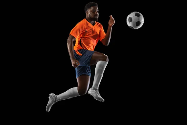 Jovem jogador de futebol africano jogando isolado em fundo preto. Conceito de esporte, movimento, energia e dinâmica. — Fotografia de Stock