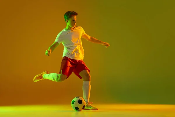 Een mannelijke voetballer in actie en beweging geïsoleerd op gradiënt groene gele achtergrond in neon licht — Stockfoto