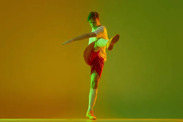 Jovem caucasiano homem, futebol masculino jogador de treinamento isolado no gradiente azul rosa fundo em luz de néon — Fotografia de Stock