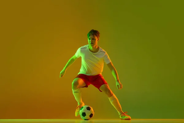 Un giocatore di calcio maschile in azione e movimento isolato su sfondo giallo verde sfumato in luce al neon — Foto Stock