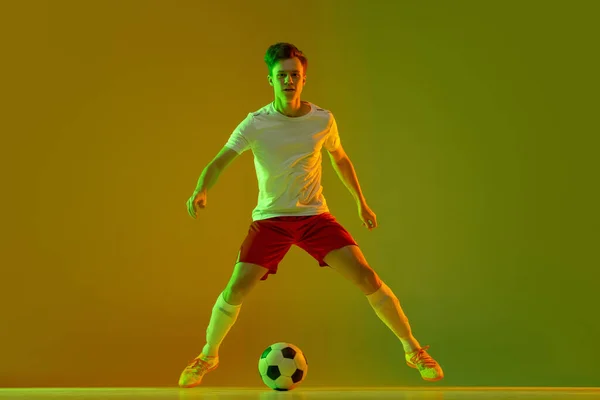 Een mannelijke voetballer in actie en beweging geïsoleerd op gradiënt groene gele achtergrond in neon licht — Stockfoto