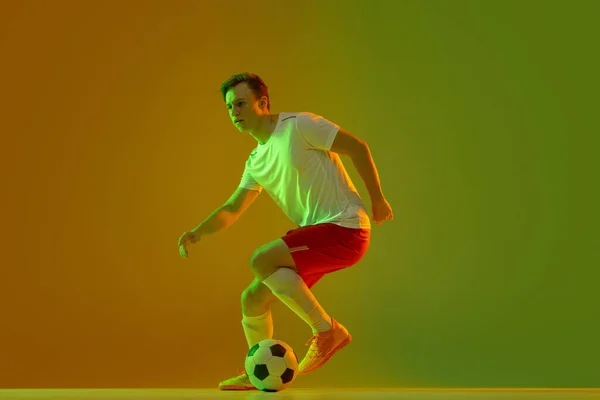 Un footballeur masculin en action et en mouvement isolé sur fond jaune vert dégradé au néon — Photo