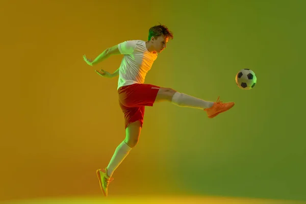 Egy férfi labdarúgó labdarúgó akció közben és mozgás elszigetelt gradiens zöld sárga háttér neon fény — Stock Fotó