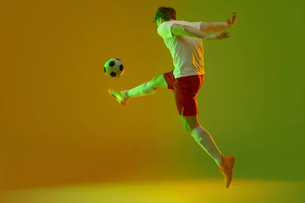 Hombre joven caucásico, entrenamiento de jugador de fútbol masculino aislado sobre fondo rosa azul degradado en luz de neón — Foto de Stock