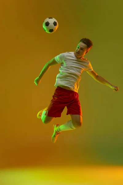 Young caucasian man, male soccer football player training isolated on gradient yellow green background in neon light — Stock Photo, Image