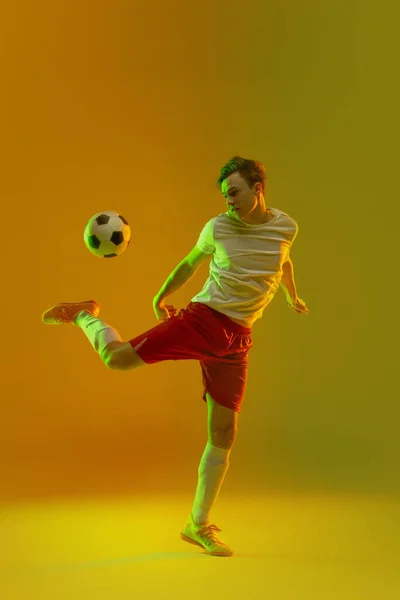 Un giocatore di calcio maschile in azione e movimento isolato su sfondo giallo verde sfumato in luce al neon — Foto Stock