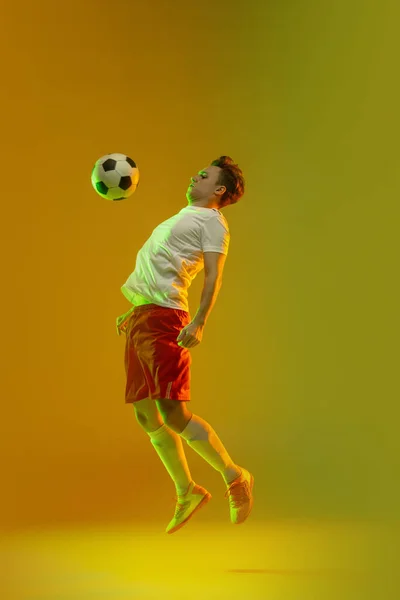 Jeune homme caucasien, joueur de football masculin s'entraînant isolé sur fond vert jaune dégradé au néon — Photo