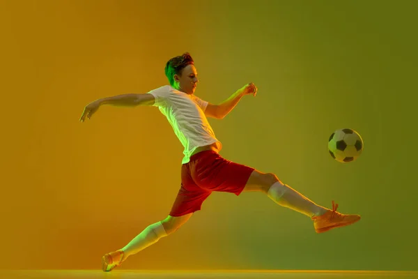 Um jogador de futebol masculino em ação e movimento isolado em gradiente verde fundo amarelo em luz de néon — Fotografia de Stock