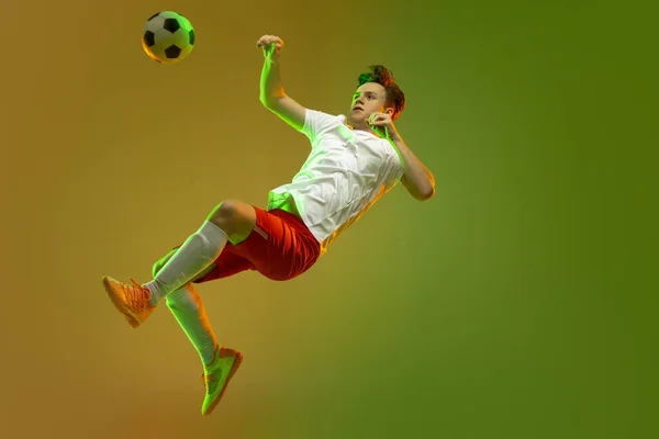 Mladý běloch muž, mužský fotbal fotbalista trénink izolované na gradient žluté zelené pozadí v neonovém světle — Stock fotografie