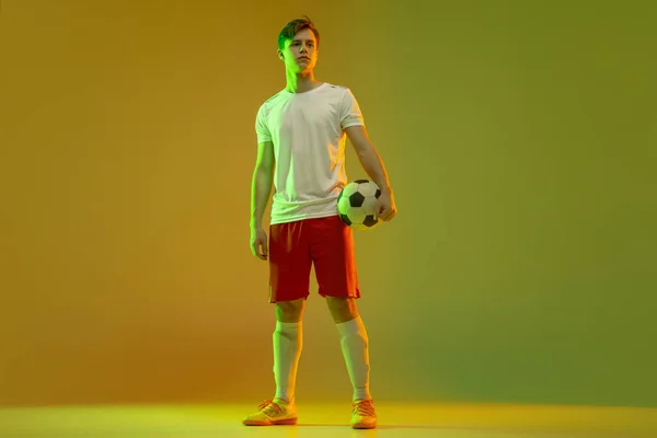 Retrato de medio cuerpo del futbolista profesional parado aislado sobre fondo verde amarillo degradado en luz de neón. Concepto de deporte, belleza. — Foto de Stock