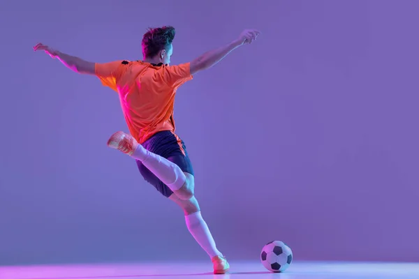一名男子足球运动员在霓虹灯下在梯度紫丁香粉红背景下的动作和动作 — 图库照片