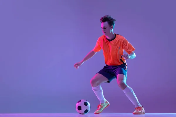 Un giocatore di calcio maschile in azione e movimento isolato su sfondo rosa lilla sfumato in luce al neon — Foto Stock