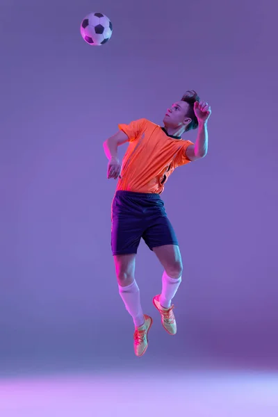 Jonge blanke man, mannelijke voetbal speler training geïsoleerd op gradiënt blauw roze achtergrond in neon licht — Stockfoto