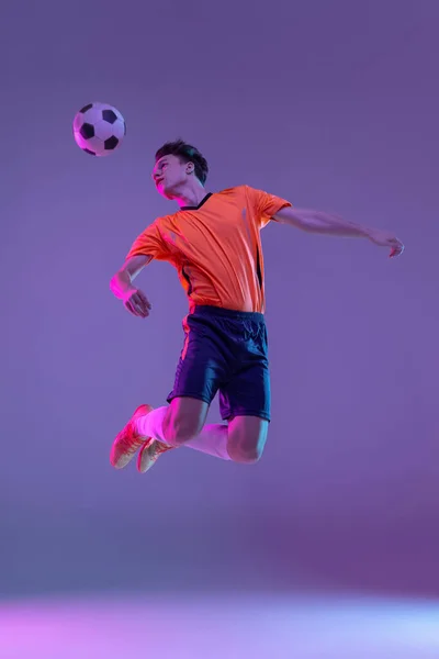 Νεαρός καυκάσιος άνδρας, αρσενικό ποδόσφαιρο ποδοσφαιριστής προπόνηση απομονώνονται σε κλίση μπλε ροζ φόντο σε νέον φως — Φωτογραφία Αρχείου