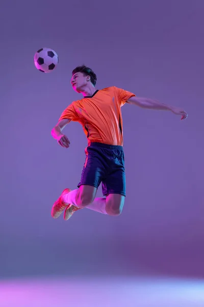 Jovem caucasiano homem, futebol masculino jogador de treinamento isolado no gradiente azul rosa fundo em luz de néon — Fotografia de Stock