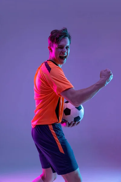 Halve lengte portret van professionele voetballer geïsoleerd op gradiënt blauw roze achtergrond in neon licht. Begrip sport, schoonheid. — Stockfoto