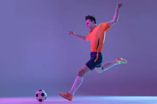 Een mannelijke voetballer in actie en beweging geïsoleerd op gradiënt lila roze achtergrond in neon licht — Stockfoto