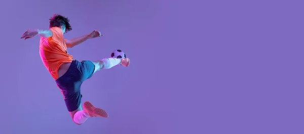 Jonge blanke man, mannelijke voetbal speler training geïsoleerd op gradiënt blauw roze achtergrond in neon licht — Stockfoto