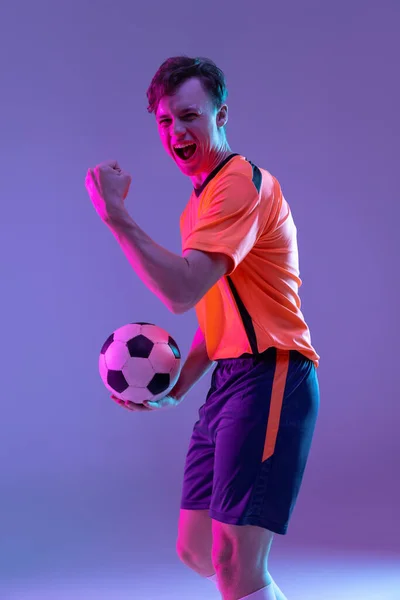 Halve lengte portret van professionele voetballer geïsoleerd op gradiënt blauw roze achtergrond in neon licht. Begrip sport, schoonheid. — Stockfoto
