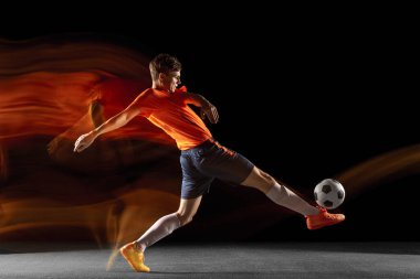 Genç beyaz erkek futbolcu ya da futbolcu koyu arkaplanda karışık ışık altında topa vuruyor. Sağlıklı yaşam tarzı, profesyonel spor, hobi kavramı.