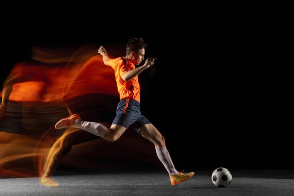 Молодой кавказский футболист или футболист бьет мячом по воротам в смешанном свете на темном фоне. Концепция здорового образа жизни, профессионального спорта, хобби. — стоковое фото