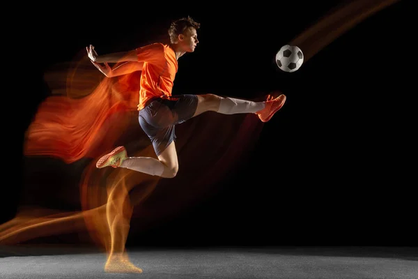 Jonge Kaukasische mannelijke voetbal of voetballer schoppen bal voor het doel in gemengd licht op donkere achtergrond. Concept van gezonde levensstijl, professionele sport, hobby. — Stockfoto