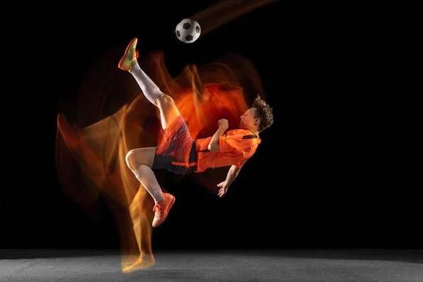 Молодой кавказский футболист или футболист бьет мячом по воротам в смешанном свете на темном фоне. Концепция здорового образа жизни, профессионального спорта, хобби. — стоковое фото