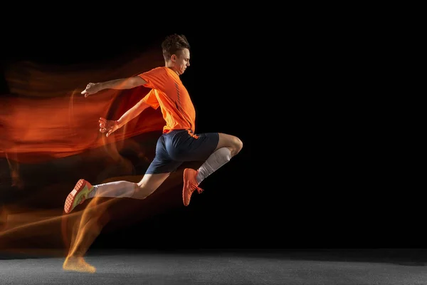 Jovem caucasiano de futebol masculino ou jogador de futebol chutando bola para o gol em luz mista sobre fundo escuro. Conceito de estilo de vida saudável, esporte profissional, hobby. — Fotografia de Stock