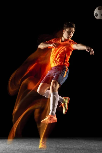 Muda sepak bola laki-laki kaukasia atau pemain sepak bola menendang bola untuk gol dalam campuran cahaya pada latar belakang gelap. Konsep dari gaya hidup sehat, olahraga profesional, hobi. — Stok Foto