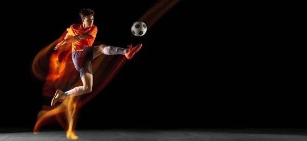 Jeune caucasien football masculin ou joueur de football coup de pied pour le but dans la lumière mélangée sur fond sombre. Concept de mode de vie sain, sport professionnel, passe-temps. — Photo