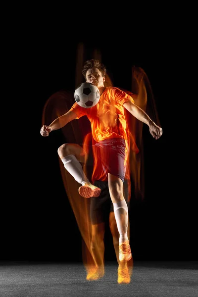 Jovem caucasiano de futebol masculino ou jogador de futebol chutando bola para o gol em luz mista sobre fundo escuro. Conceito de estilo de vida saudável, esporte profissional, hobby. — Fotografia de Stock