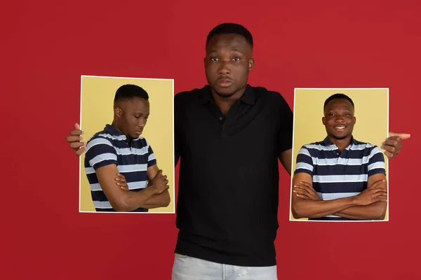 Joven africano sosteniendo sus retratos aislados sobre fondo rojo estudio con copyspace para el anuncio. —  Fotos de Stock