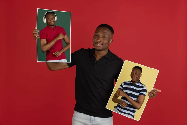 젊은 아프리카 남자가 빨간 녹음실 배경 위로 자신의 초상화를 분리하여 들고 광고를 찍는다. — 스톡 사진