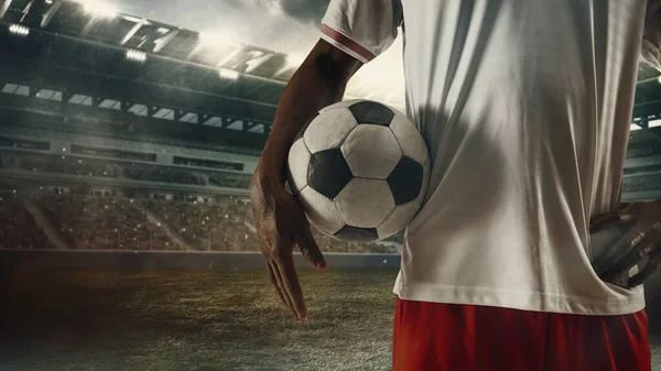 Cropped male soccer, football player standing with ball at the stadium during sport match on light sky background with flashlights. — 图库照片