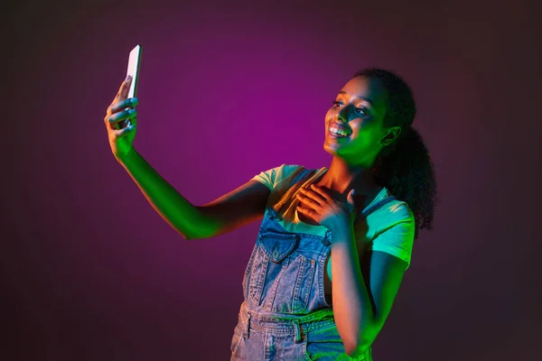 Latino young woman with phone isolated on studio background in neon. Concept of human emotions, facial expression. — Stock Photo, Image