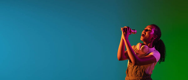 Портрет певицы-латиноамериканки изолирован на студийном фоне в неоновом свете. Красивая модель в черной одежде с микрофоном.