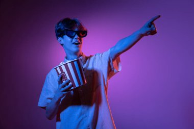 Üç boyutlu gözlüklerle ve patlamış mısırla heyecanlandım. Beyaz adamın portresi mavi stüdyo arka planında pembe neon ışıkta izole edilmiş. Güzel erkek model..