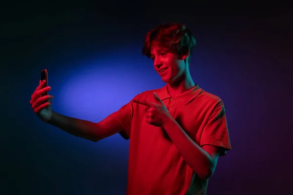 Homem jovem caucasiano com telefone isolado em fundo estúdio azul em néon. Conceito de emoções humanas, expressão facial. — Fotografia de Stock