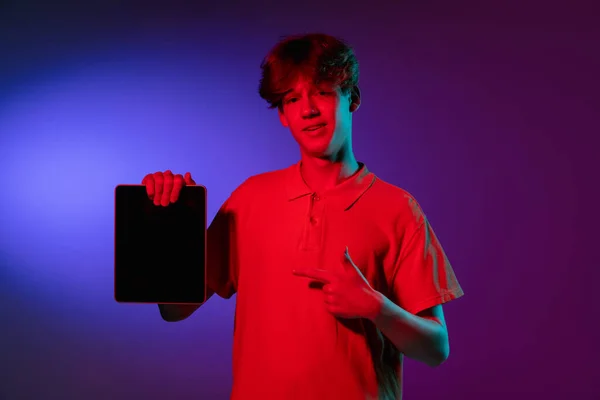 A segurar o tablet, muito excitado. Retrato de homens jovens caucasianos sobre fundo estúdio preto em luz de néon. Modelo masculino bonito em camisa branca. — Fotografia de Stock