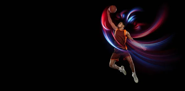Volando. Hermoso jugador de baloncesto afroamericano masculino en movimiento y acción en luz de neón sobre fondo negro. Concepto de estilo de vida saludable, deporte profesional, hobby. —  Fotos de Stock
