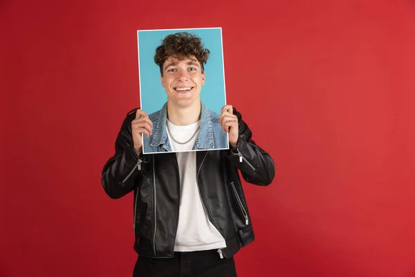 Joven sosteniendo su retrato aislado sobre fondo rojo del estudio con copyspace para el anuncio. —  Fotos de Stock